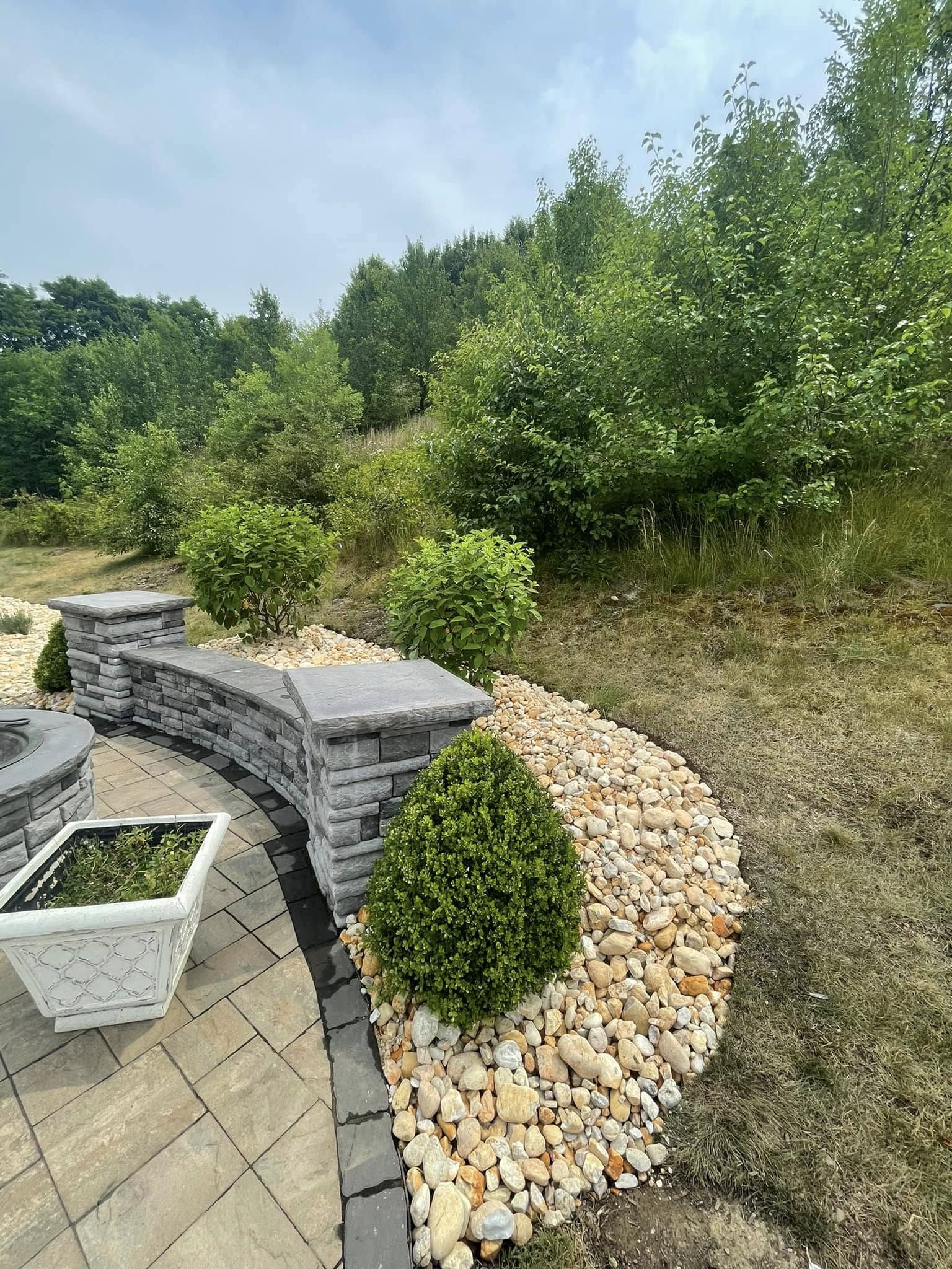 Curved paver patio with integrated seat wall, pillar caps, and decorative river rock bed