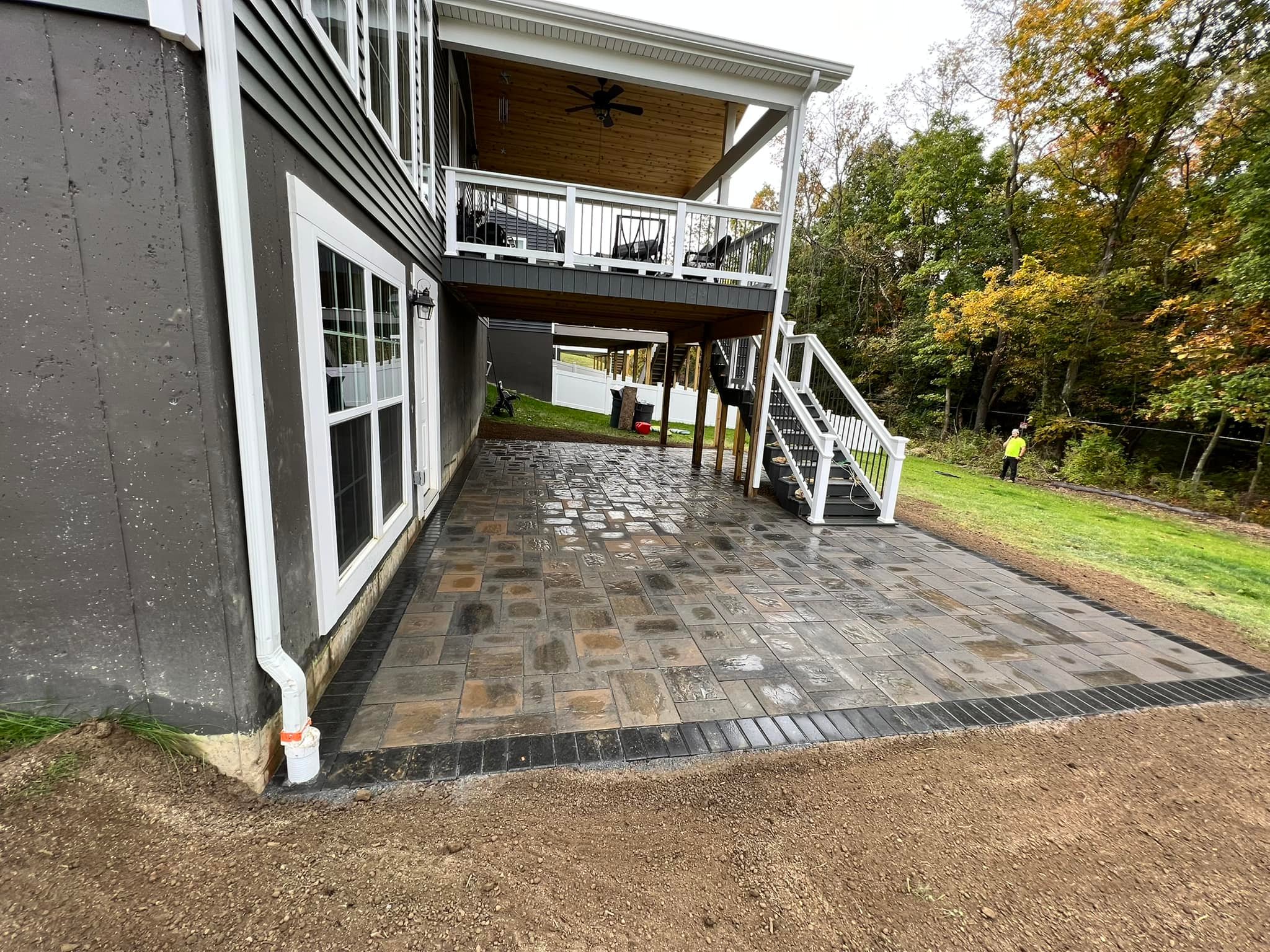 Large covered paver patio installed beneath elevated deck with multi-tone pattern