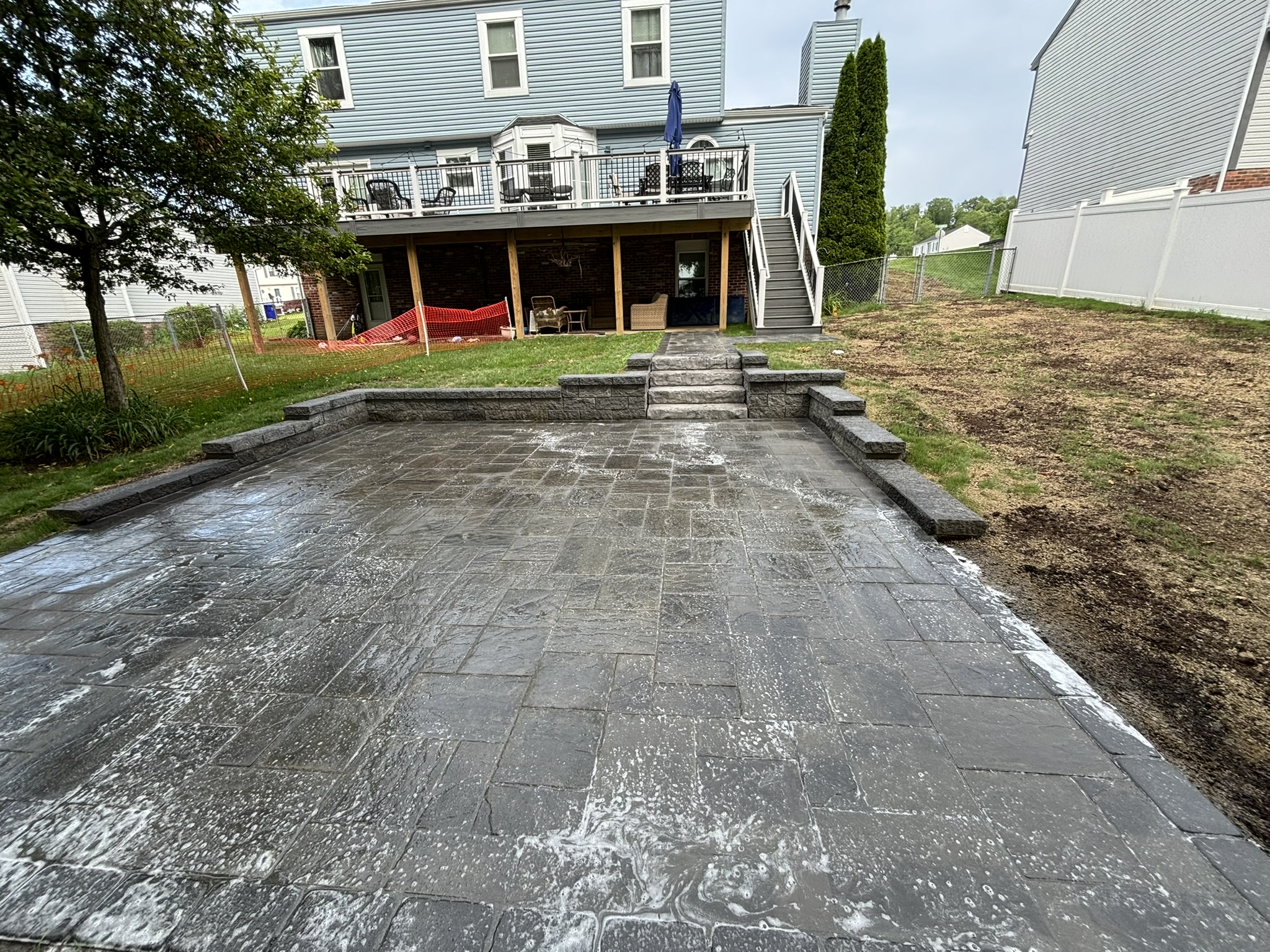 Large paver patio with retaining wall seating and integrated steps to elevated deck